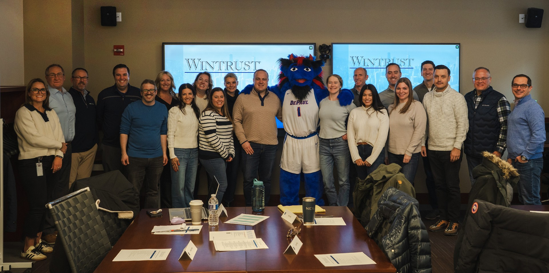 a group of professionals pose in a conference room with DePaul's mascot, DIBS